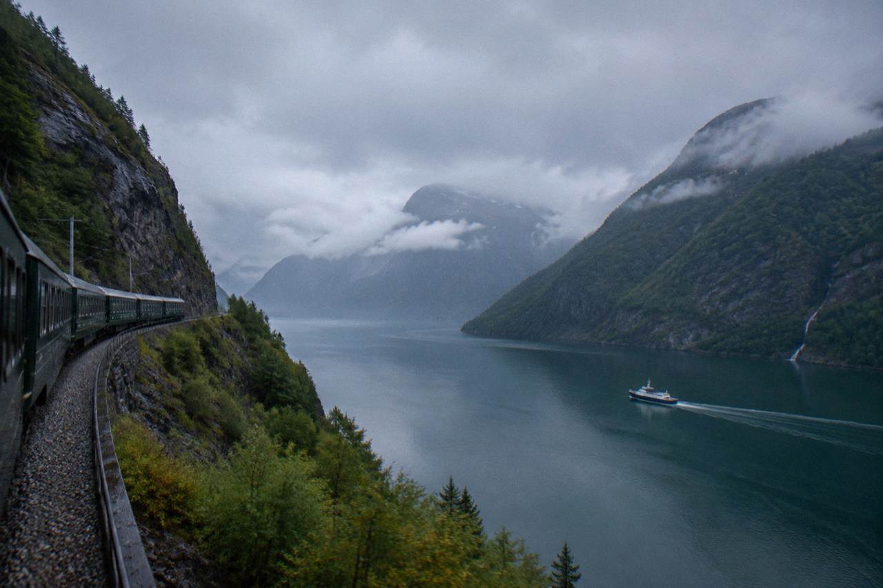 A passenger train winding along a steep mountainside above a deep Norwegian fjord