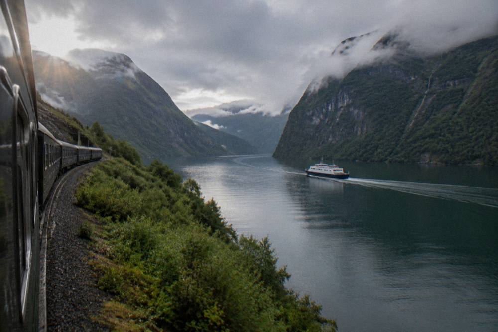 A narrow fjord boat travelling between steep mountain walls on calm water