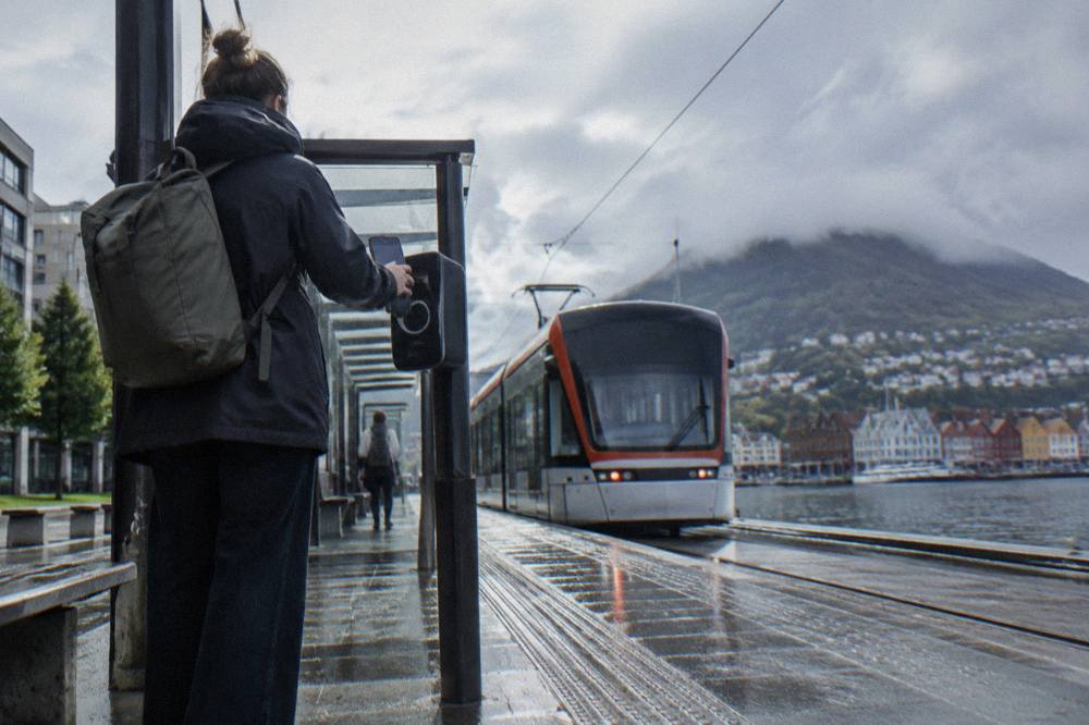 A traveller paying with a smartphone on a tram platform next to a light rail stop in central Bergen