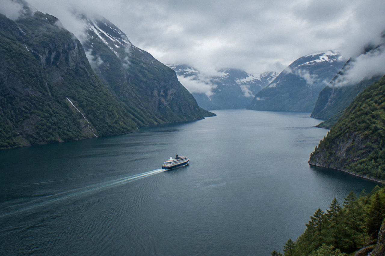 A cruise boat on a narrow Norwegian fjord with steep forested cliffs rising on both sides