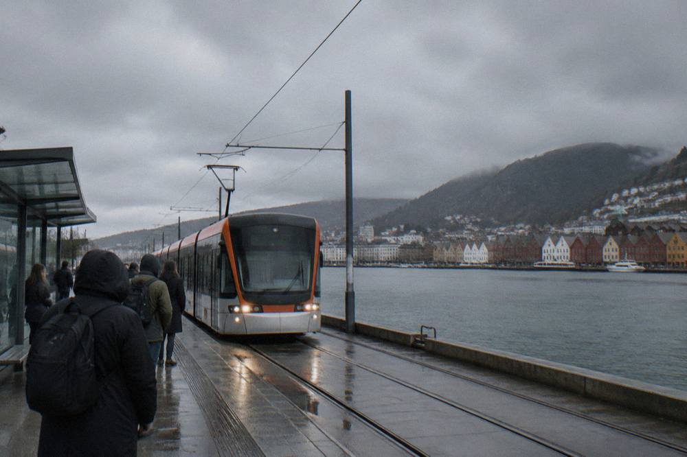 A light rail tram arriving at an outdoor platform in Bergen on an overcast day, with passengers waiting to board