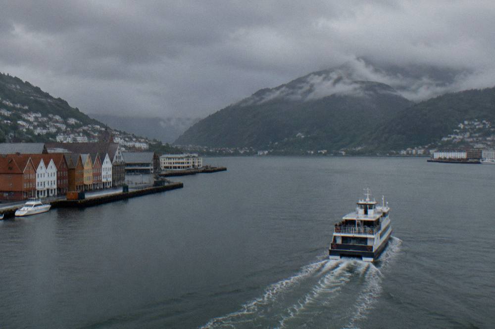 A passenger boat leaving Bergen's harbour toward steep forested hills at the mouth of a fjord
