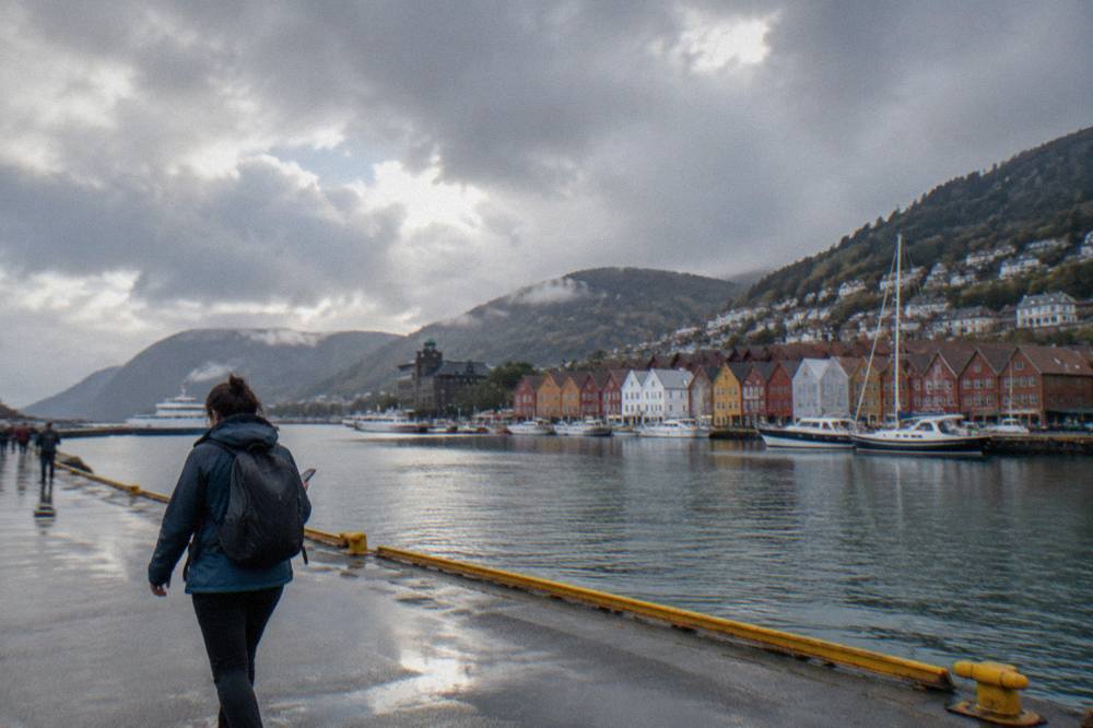 A traveller in a rain jacket checking a phone clock while walking past the harbour in Bergen