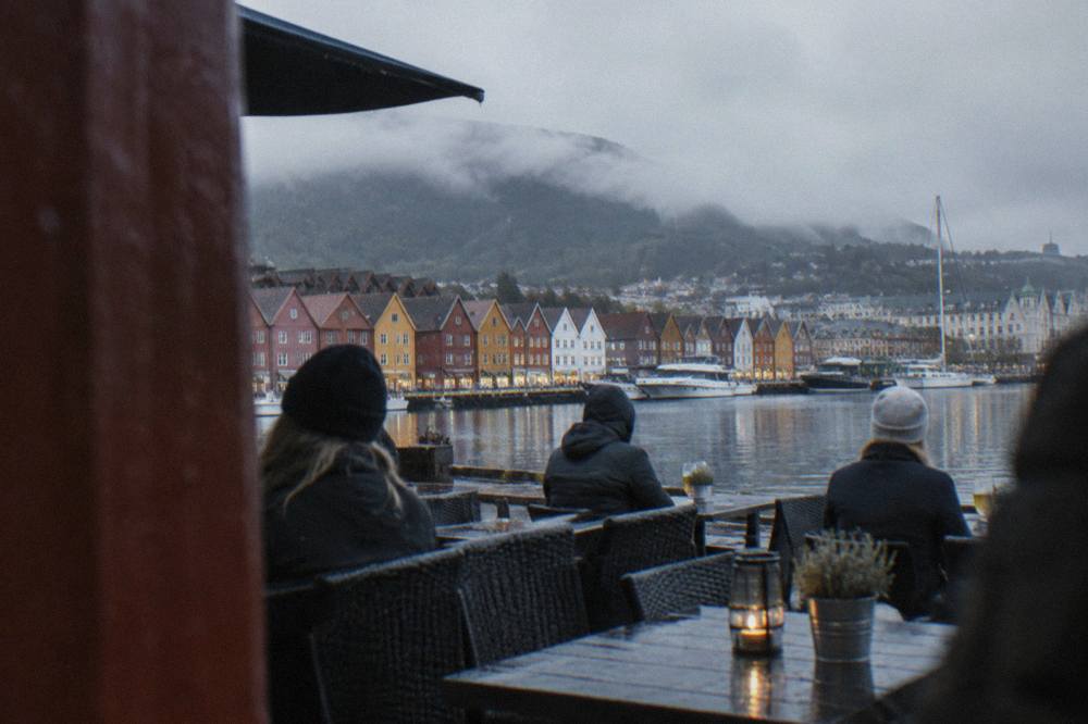 People sitting outside a bar in central Bergen with the illuminated wooden buildings of Bryggen in the background