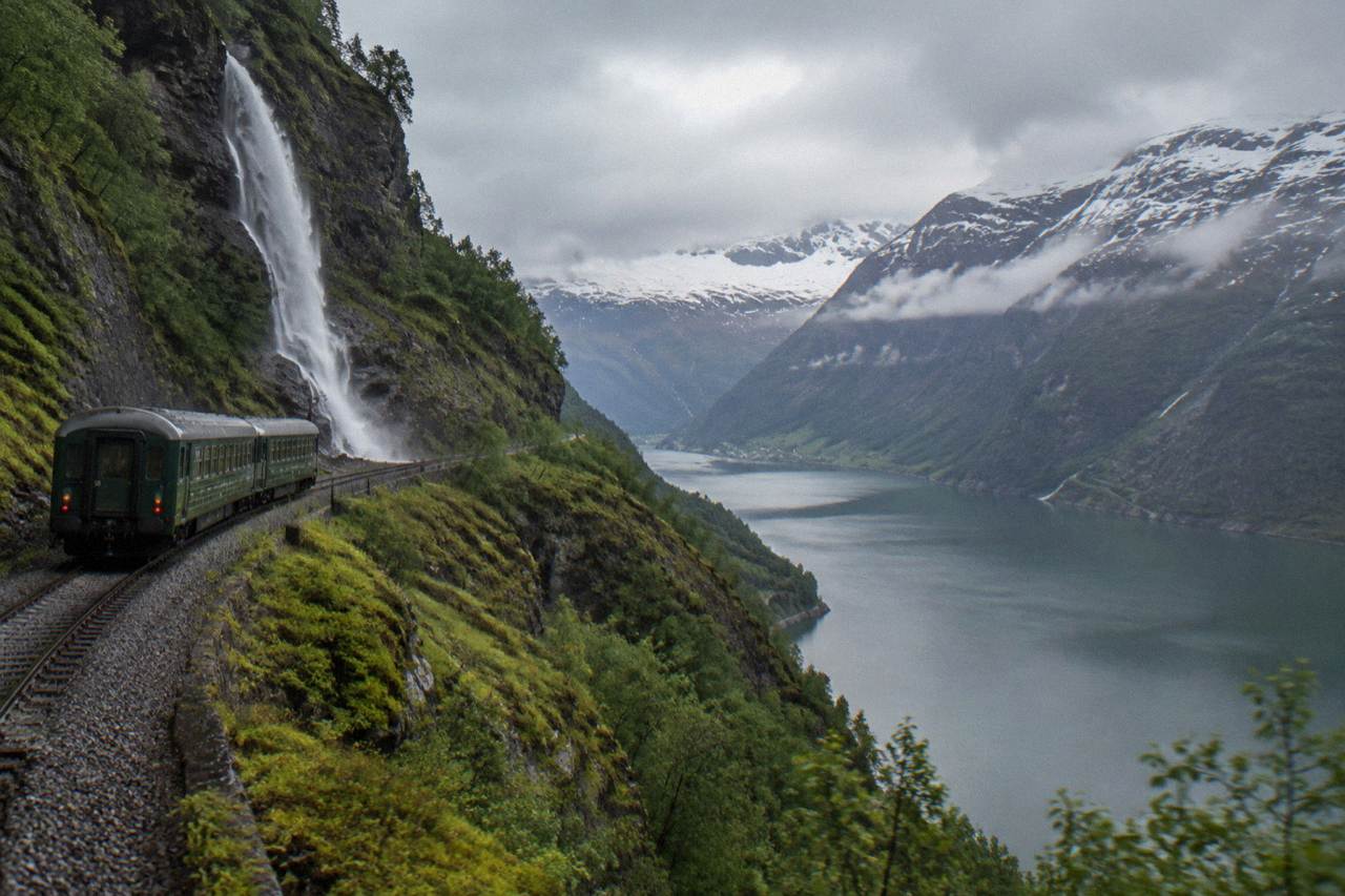 A passenger train travelling through a snow-dusted mountain plateau in Norway