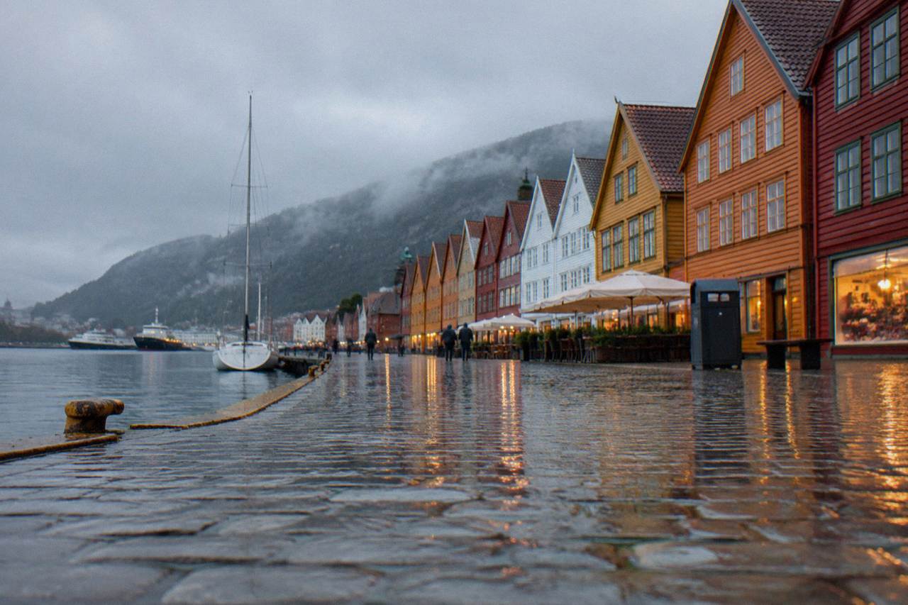 Rain-soaked colourful wooden houses along the waterfront in Bergen, Norway, with wet cobblestones reflecting the lights.
