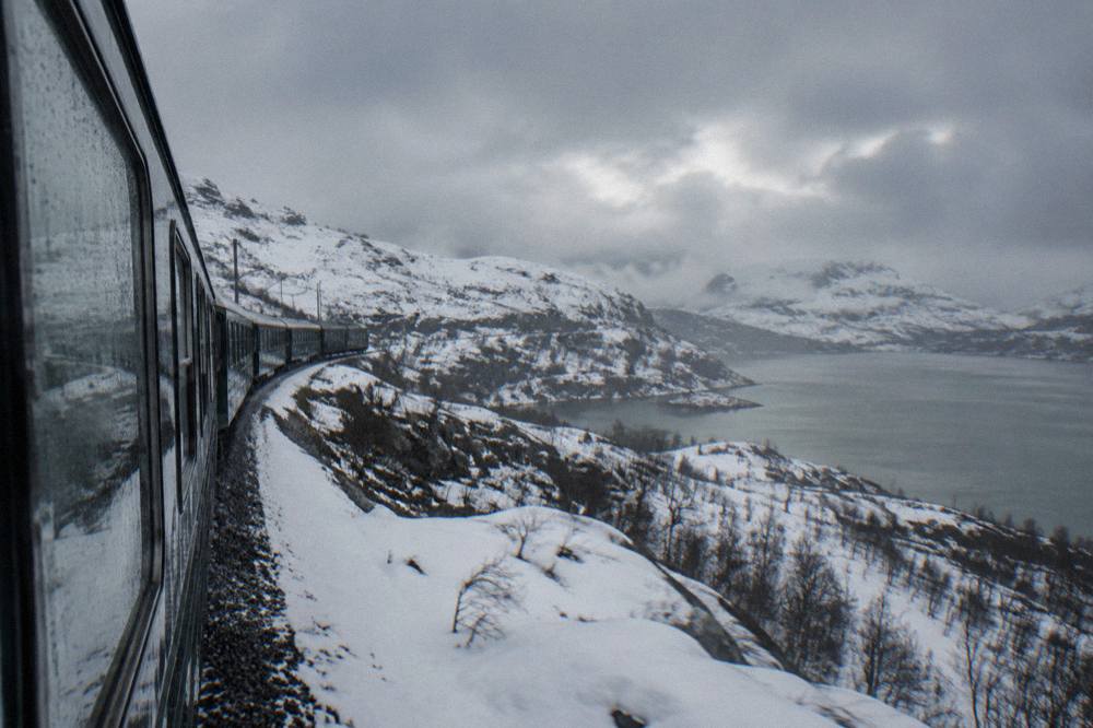 A passenger train on the Bergen Line travelling through high snow-covered open mountain country