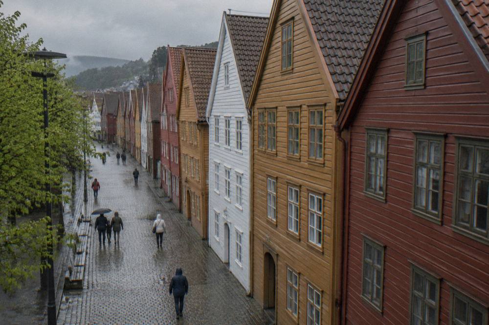 A visitor in a rain jacket walking along the wooden buildings and cobbles of Bryggen in Bergen in early spring