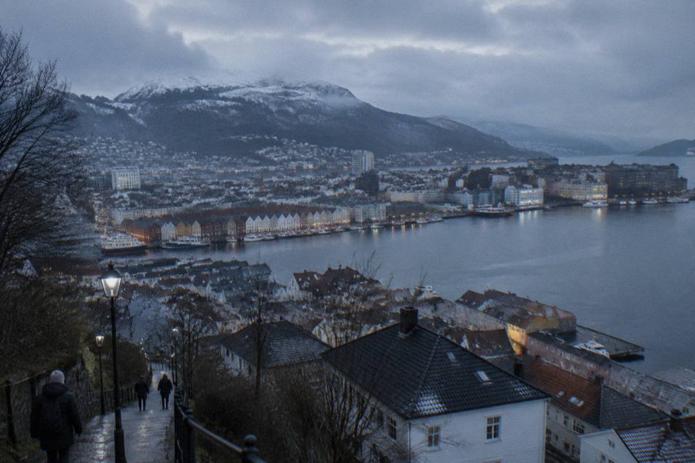 Snow-dusted mountain slopes rising above the rooftops of Bergen under a pale winter sky