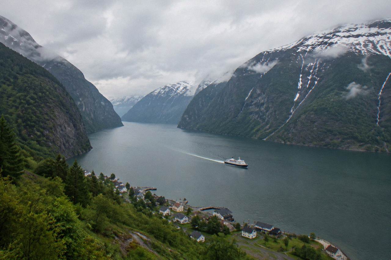 A long fjord cutting between steep forested mountains, with calm dark water and a small village at the shoreline
