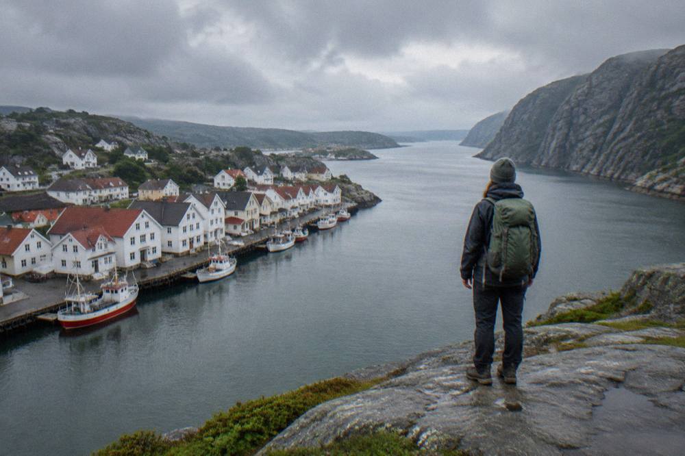 A hiker standing on a flat cliff ledge looking down over a long narrow fjord with steep rock walls