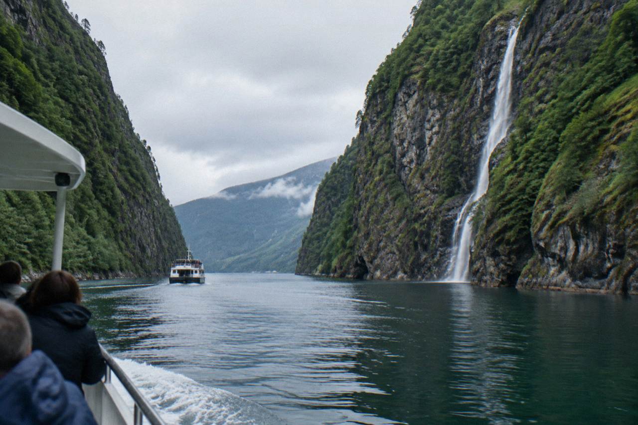 A sightseeing boat travelling along a narrow Norwegian fjord with steep forested cliffs on both sides