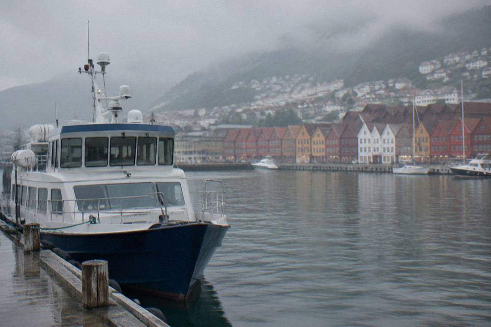 A passenger boat moored at a wooden pier in Bergen harbour with colourful buildings along the waterfront