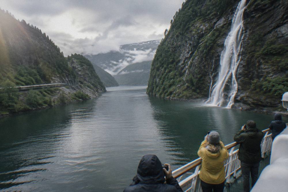 Tourists standing on the deck of a fjord cruise boat photographing a waterfall on a steep rock wall