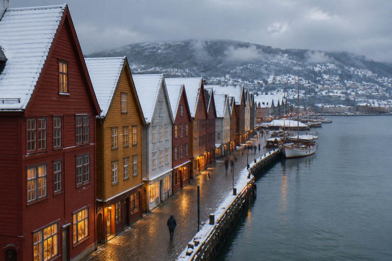 Snow-covered wooden houses on Bryggen wharf in Bergen at dusk with warm lights in the windows