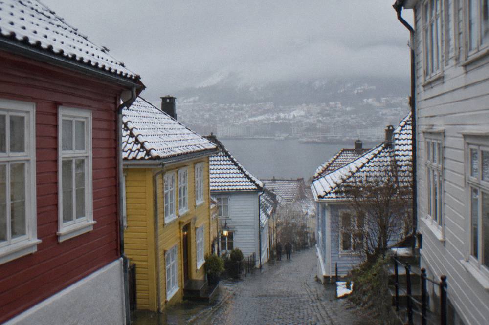 A narrow lane between colourful wooden houses in central Bergen with light snow on the rooftops