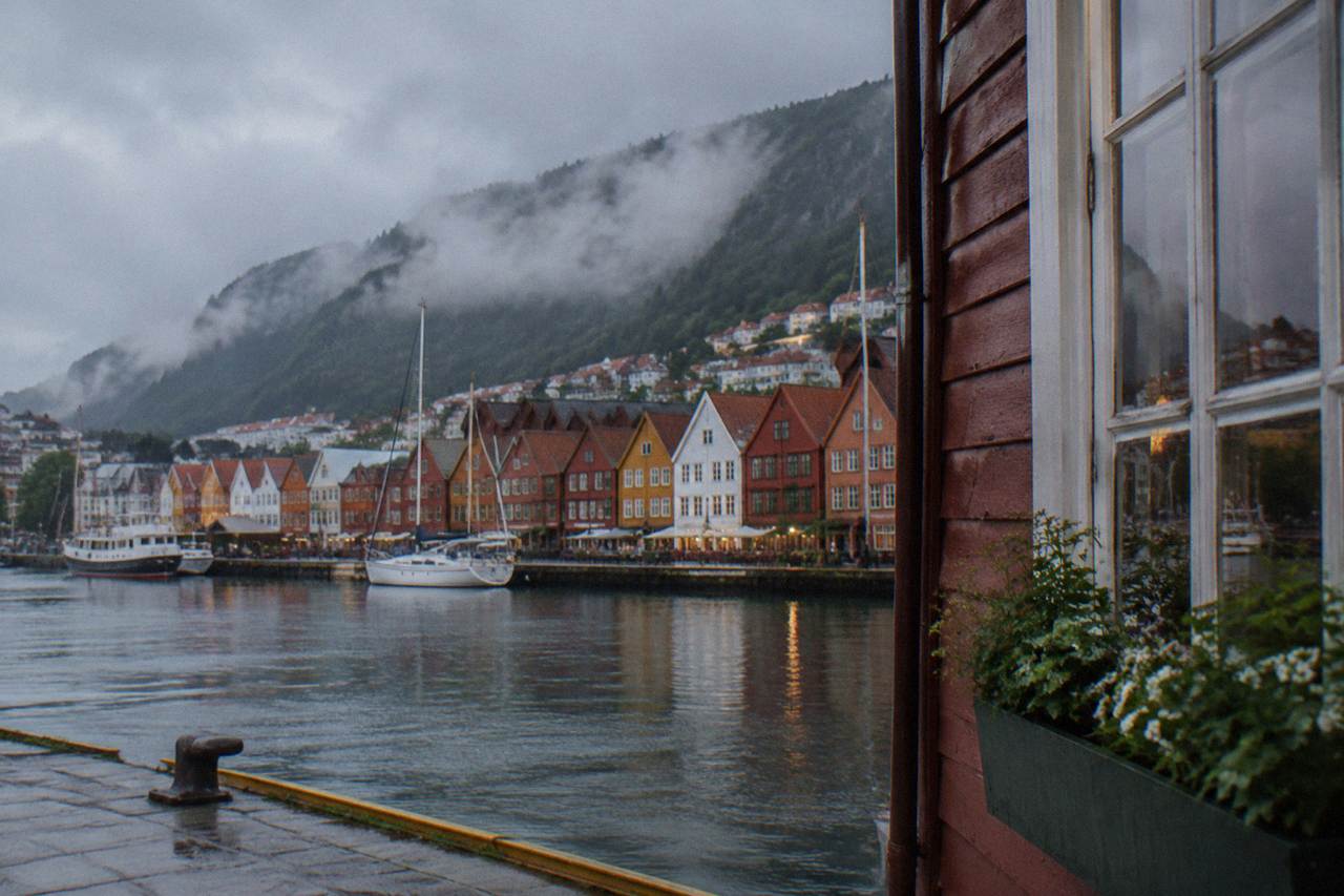 Colourful wooden houses along the waterfront of a Norwegian coastal city with steep forested mountains rising behind them