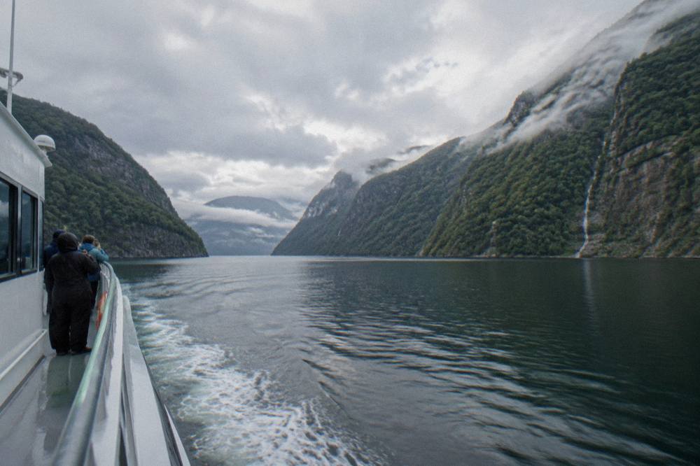 A fjord cruise boat on dark water between steep forested cliffs near Bergen