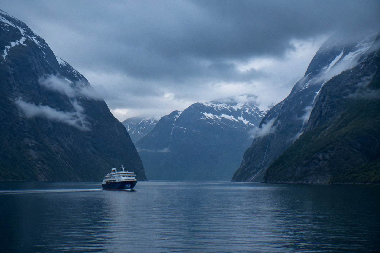 A cruise ship sailing calm water between steep fjord cliffs in western Norway