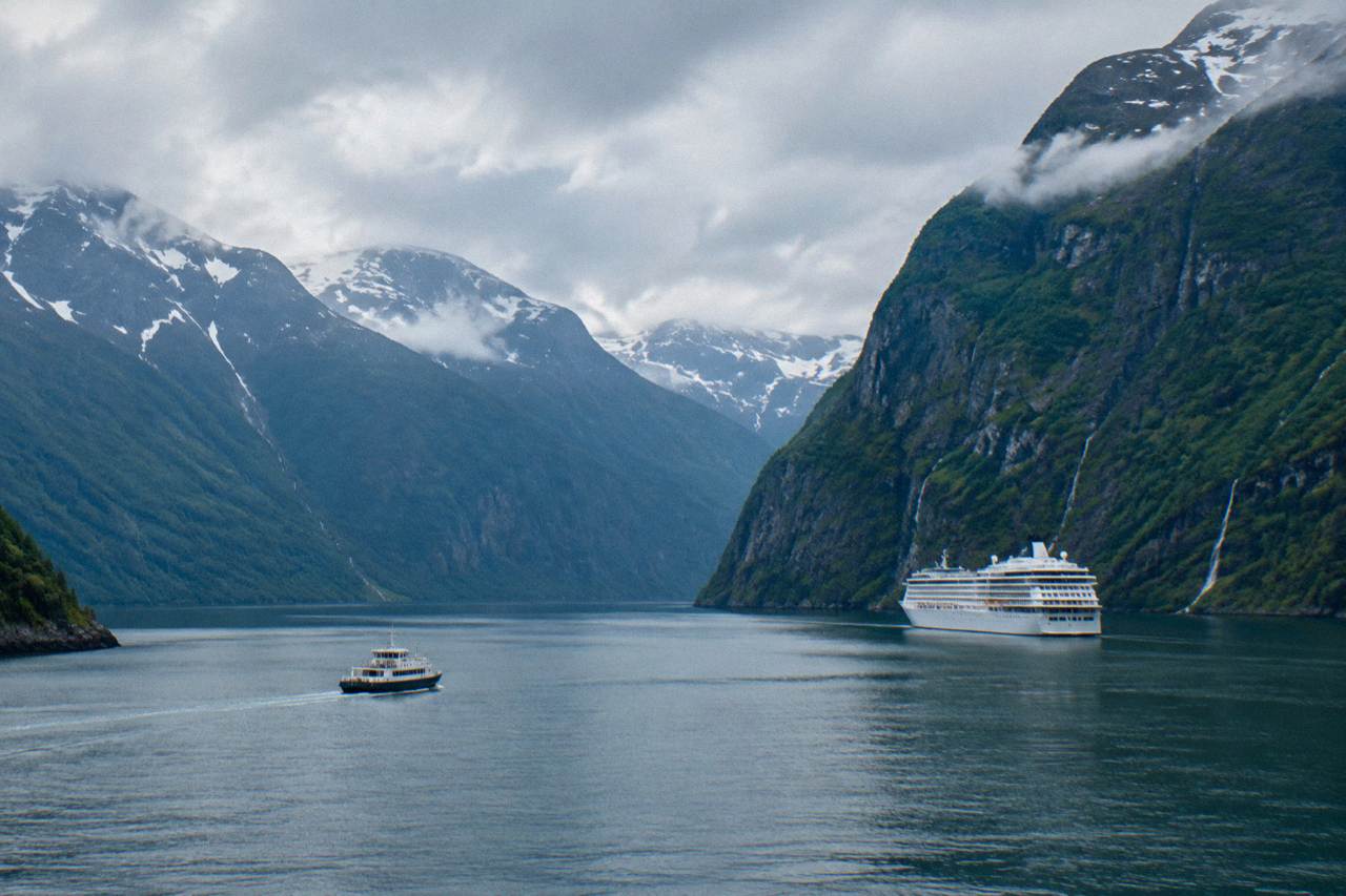 A cruise ship sailing calm water between steep green fjord cliffs in western Norway