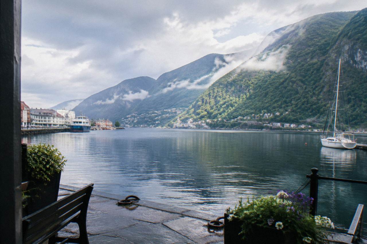 A calm fjord arm reflecting steep green mountains under a bright summer sky near Bergen