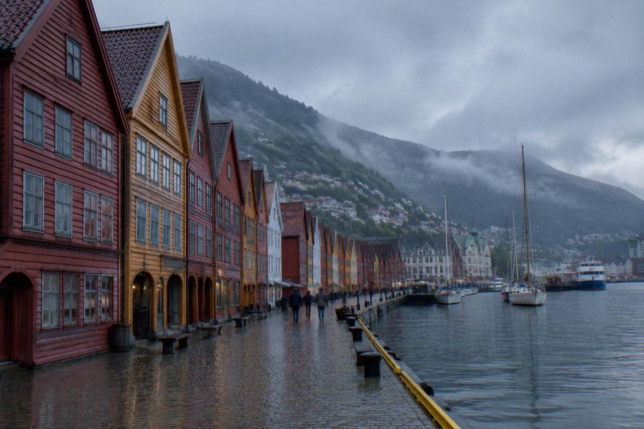 Colourful wooden Hanseatic houses along the Bryggen wharf in Bergen, with the harbour and steep green hillsides behind them