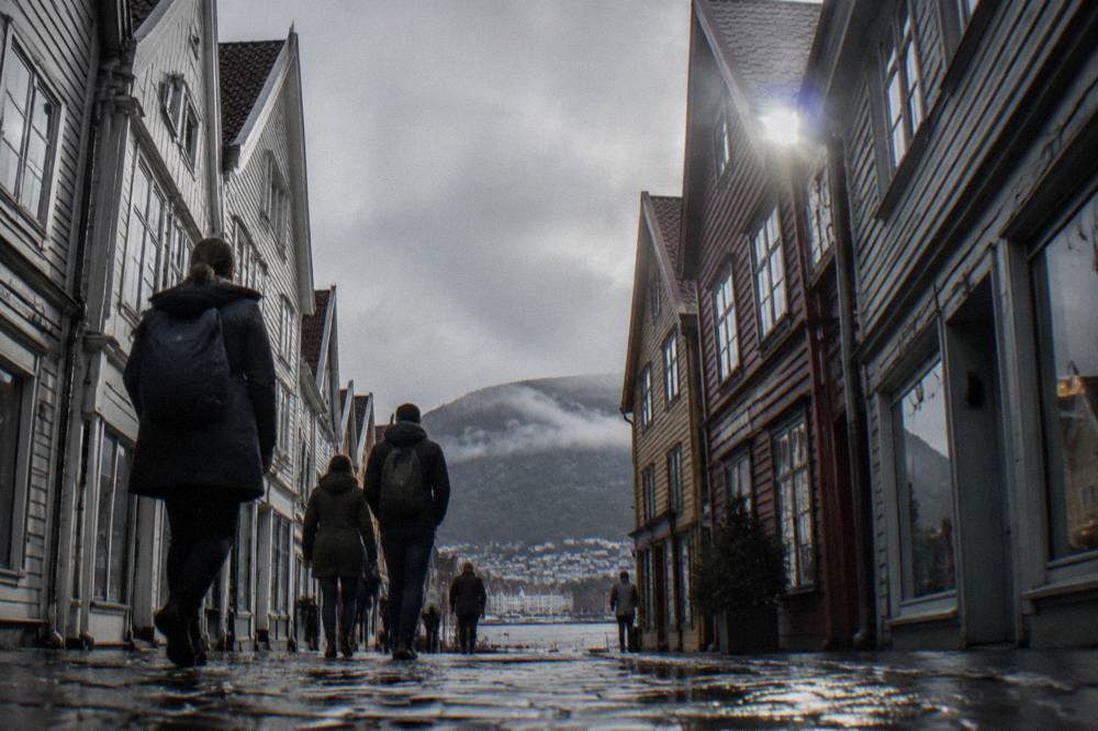 People walking through a narrow pedestrian shopping street in central Bergen, with old gabled buildings on both sides