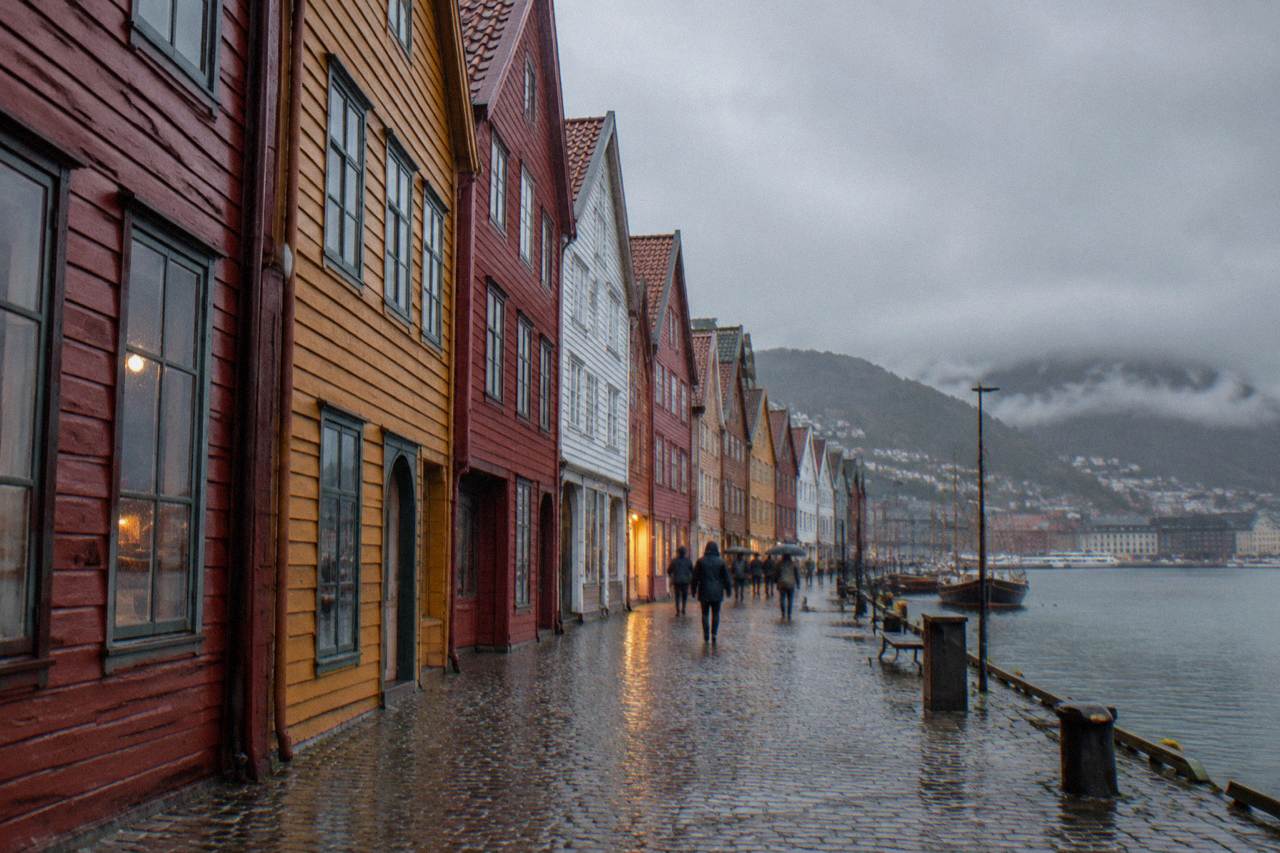 Rain falling over the colorful wooden buildings of Bryggen wharf in Bergen, with wet cobblestones reflecting the lights