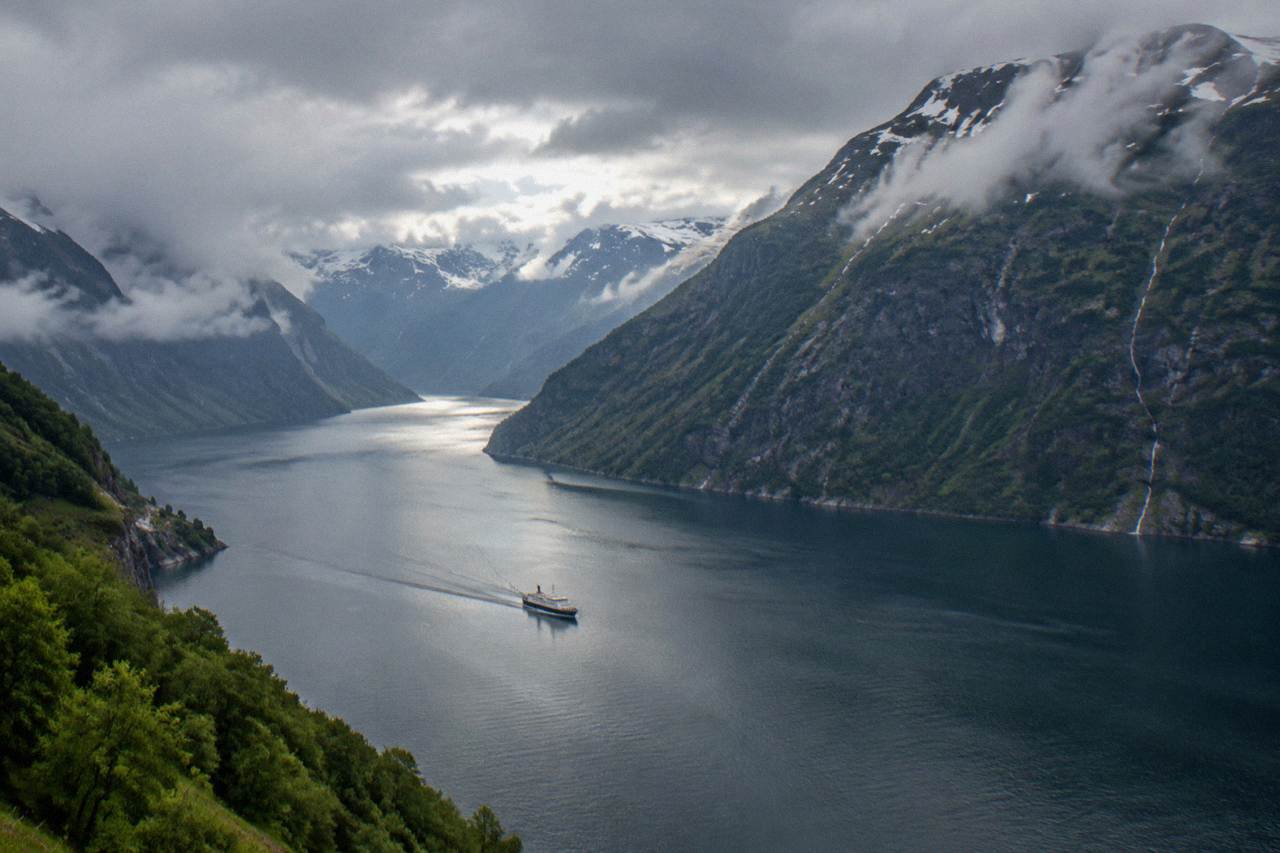 Rain clouds parting over a Norwegian fjord with steep green mountainsides and calm water below