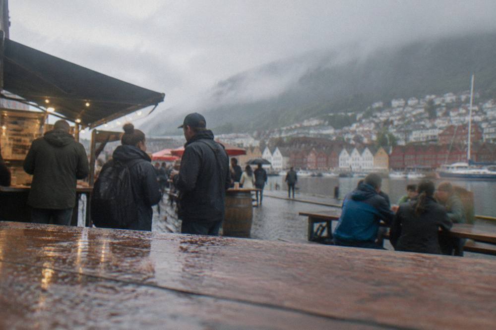 Locals and visitors talking at an outdoor food stall in central Bergen on a mild evening