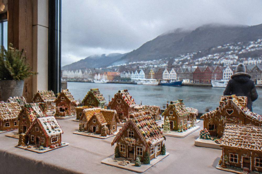 A table of small decorated gingerbread houses displayed indoors in Bergen