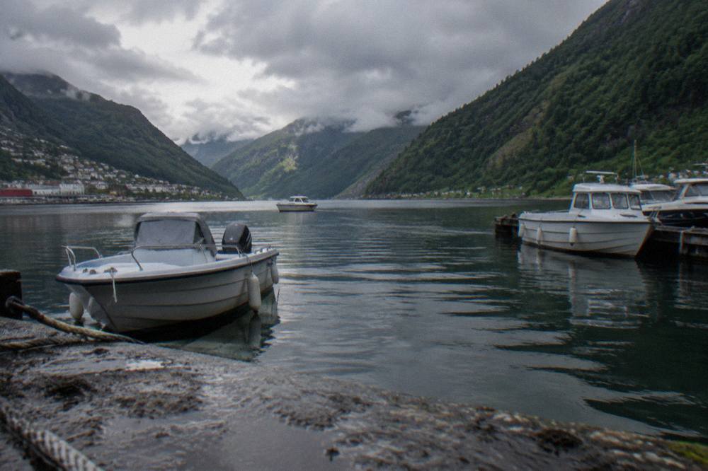 Small boats moored in a Norwegian fjord inlet with steep green mountainsides rising on both sides