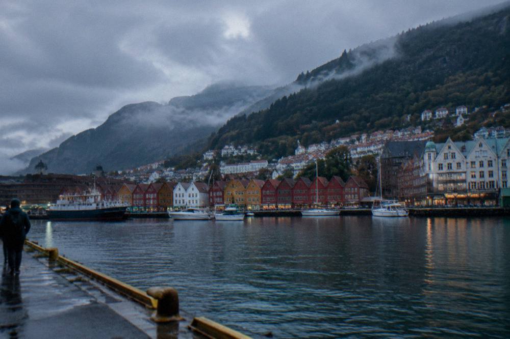 A fjord-side view of Bergen with steep forested mountains rising behind the coloured houses of the city centre
