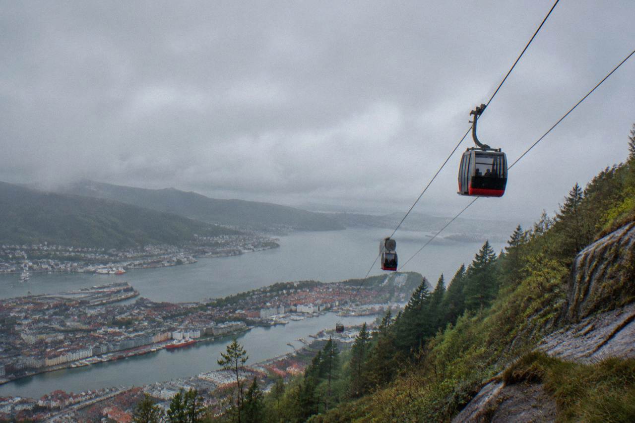Two cable car cabins travelling up a steep mountainside above a Norwegian coastal city