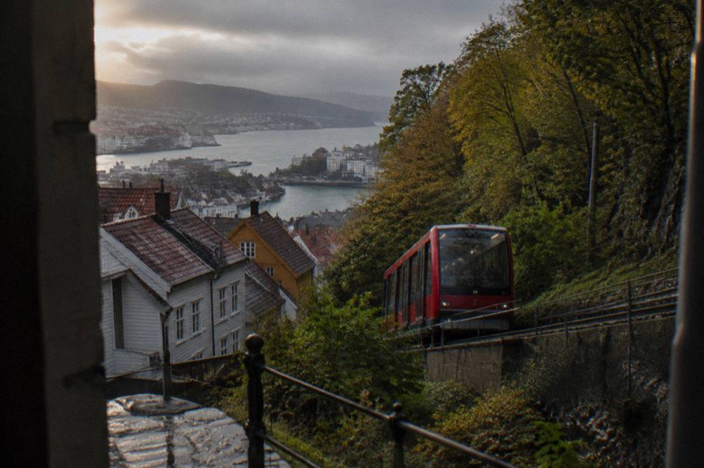 A red funicular carriage climbing a wooded hillside beside a Scandinavian timber town