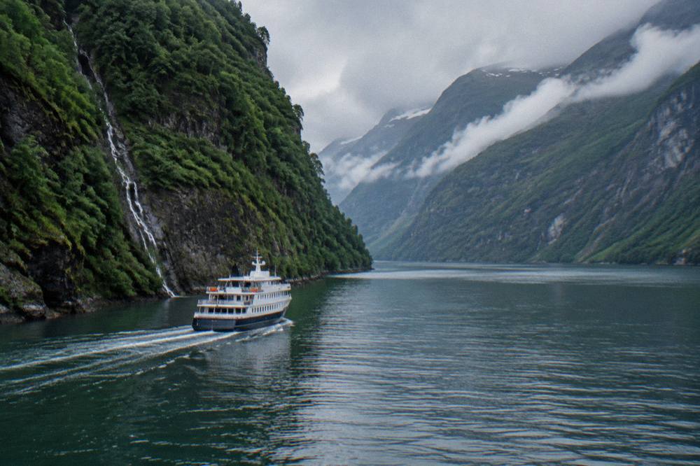 A small cruise boat on a narrow fjord between steep green cliffs near Flam