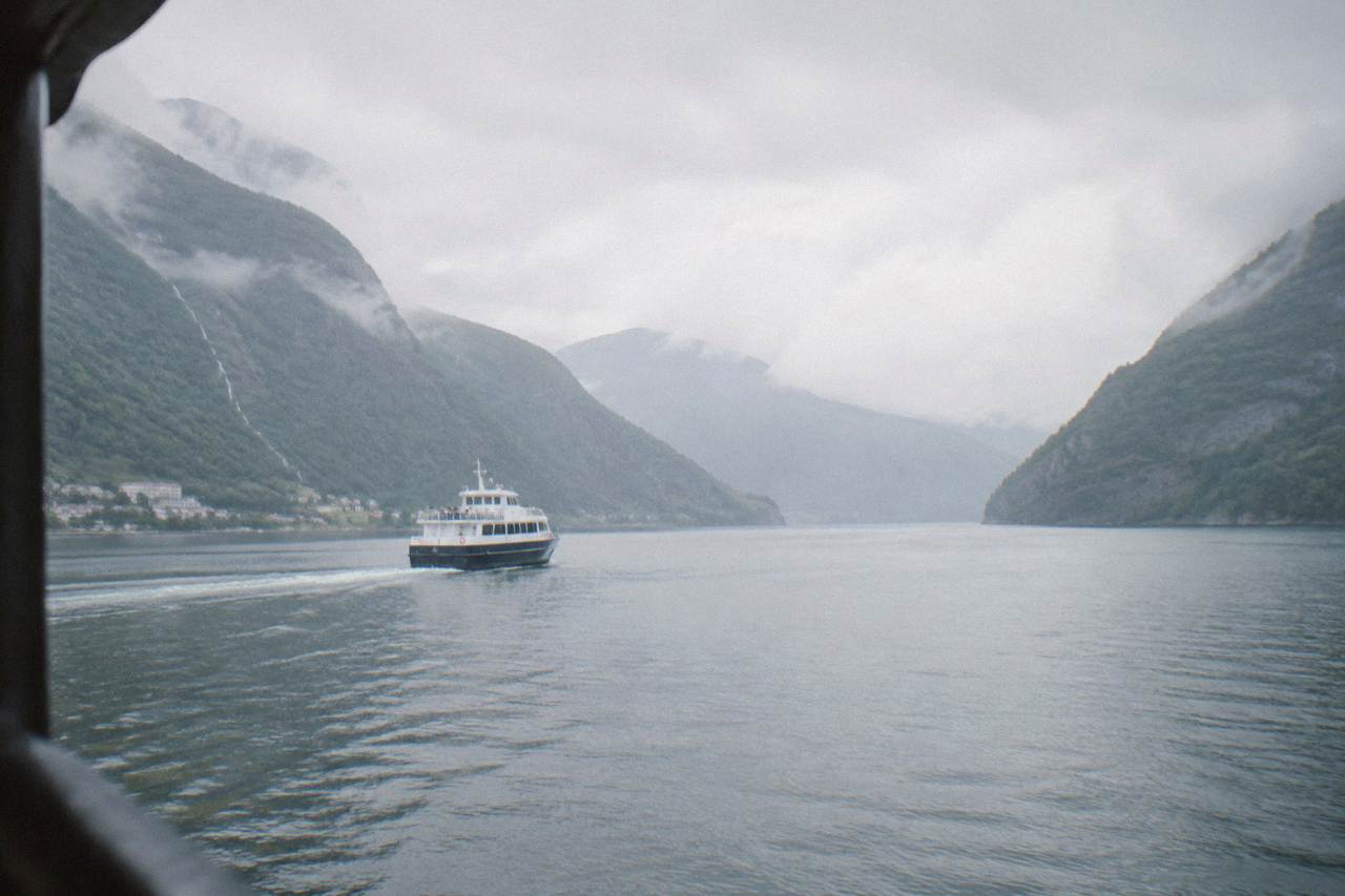 A passenger boat travelling on a wide Norwegian fjord with steep forested mountains rising on both sides