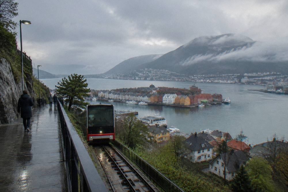 A steep mountain railway platform beside a fjord with a small village of colourful buildings at the water's edge