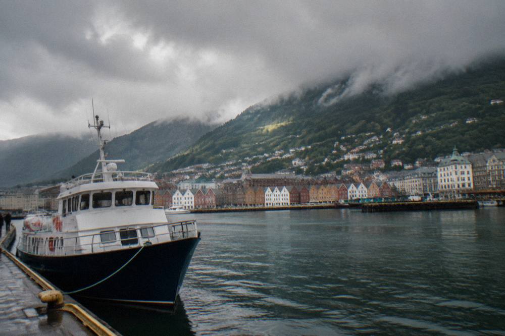 A fjord boat moored in Bergen's harbour with steep green mountains rising behind the city