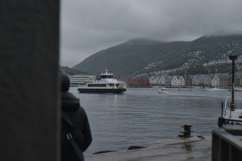 A passenger ferry and small boats on the water in Bergen harbour with green hills behind