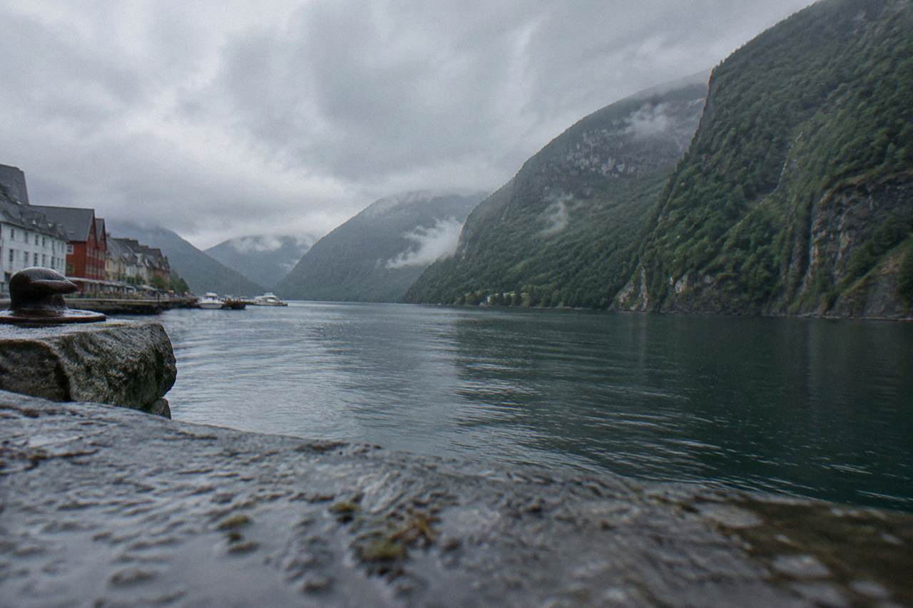 A narrow fjord with steep green cliffs and calm dark water under low clouds