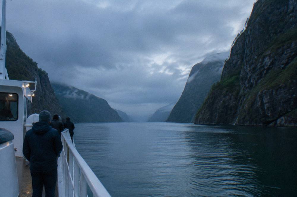 A tour boat entering a narrow fjord strait with cliffs rising on both sides