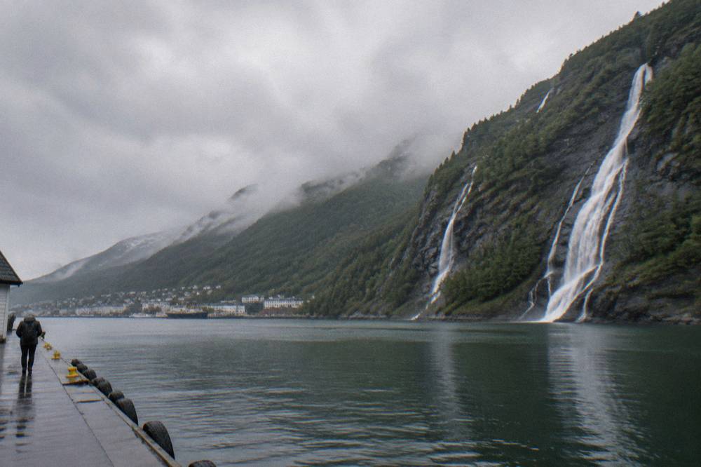 Waterfalls tumbling down a dark rock face toward still fjord water