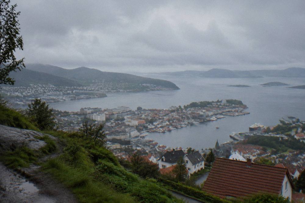 View from a mountain above Bergen across red rooftops, the harbour and islands in the sea beyond on a soft light day