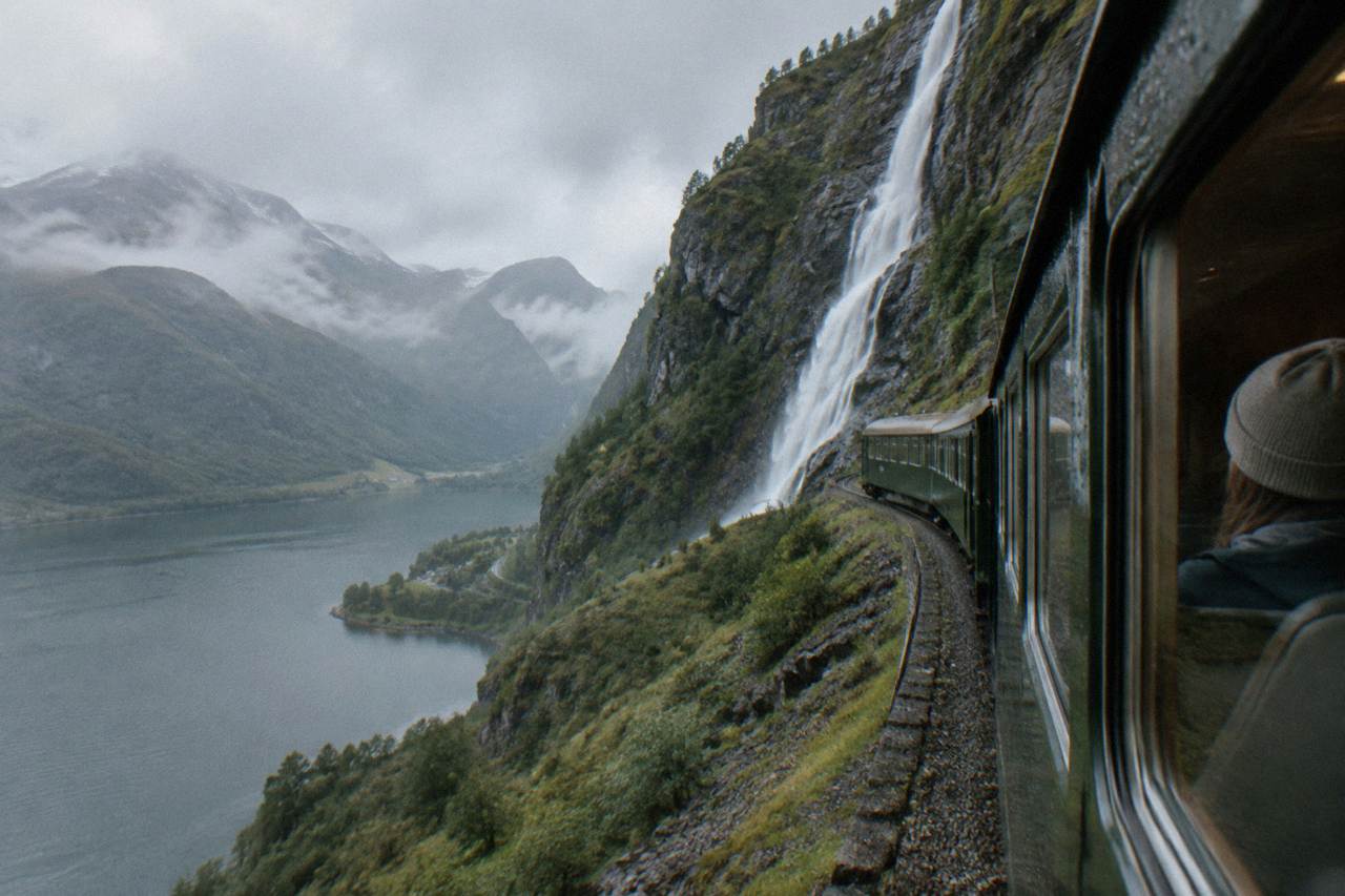 A passenger seated at a window on a Norwegian mountain railway, watching moorland and lakes pass by.