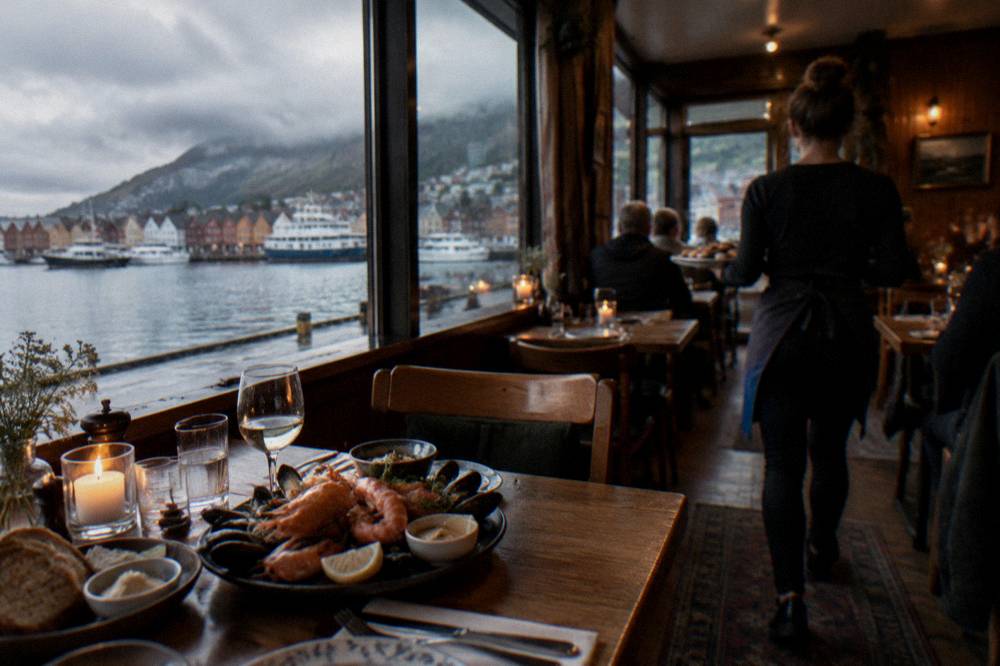 A cozy interior of a small Bergen restaurant with wooden tables, candles and plates of seafood being served