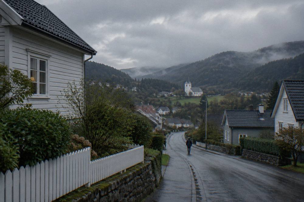 A quiet residential street with wooden houses and green gardens under an overcast sky