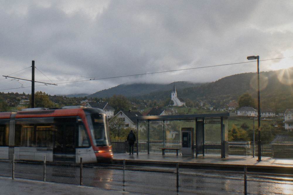 A light rail tram passing a modern stop with shelter and ticket machines
