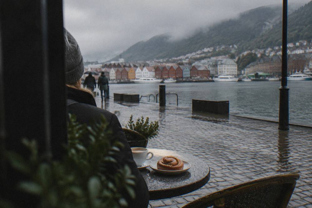 Cafe table with coffee and a cinnamon bun beside a cobbled street in Bergen