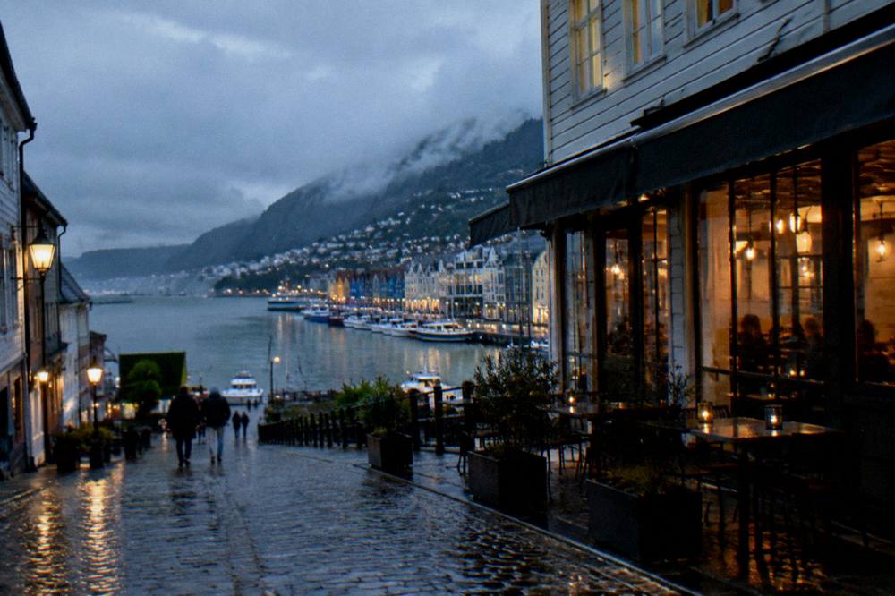 Evening light on cobbled lanes with cafe windows lit in central Bergen